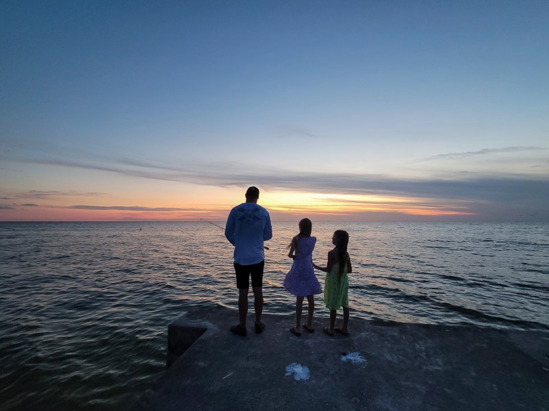 A dad and his daughters fishing at the pier at Cortez Beach, Bradenton Beach, Florida. 