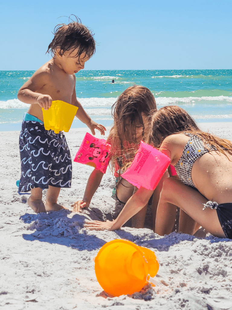 Kids playing at the beach in the sand with beach toys and floaties.