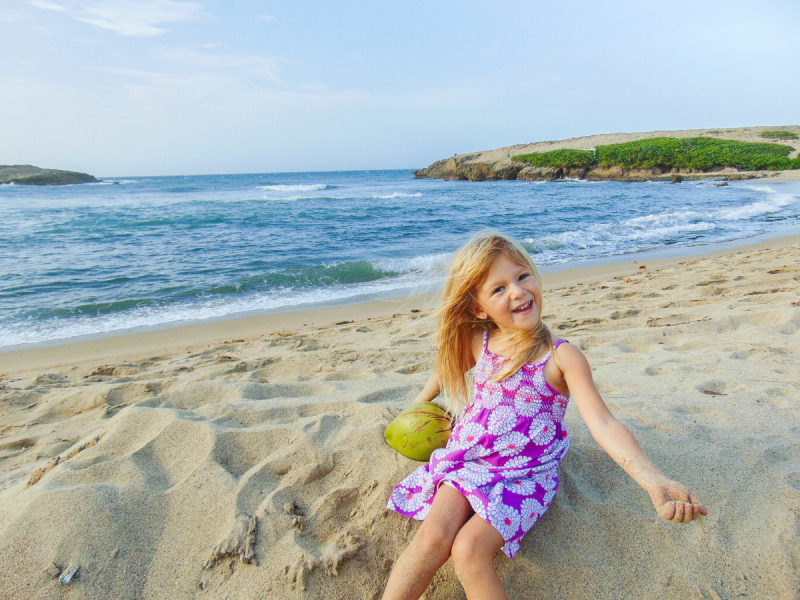 a little girl playing at the beach with a coconut