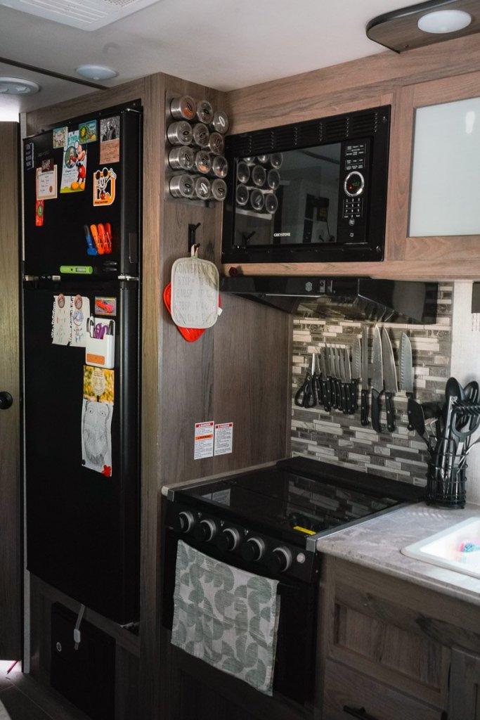 camper kitchen wall storage ideas. Showcasing a wall mounted magnetic knife rack and a seasoning rack along with a hook for hanging oven mitts.