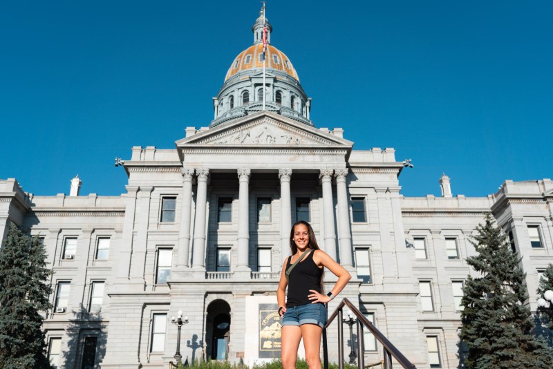 A woman standing in front of the state capitol of Colorado located in the historical neighborhood of Denver, Colorado. 