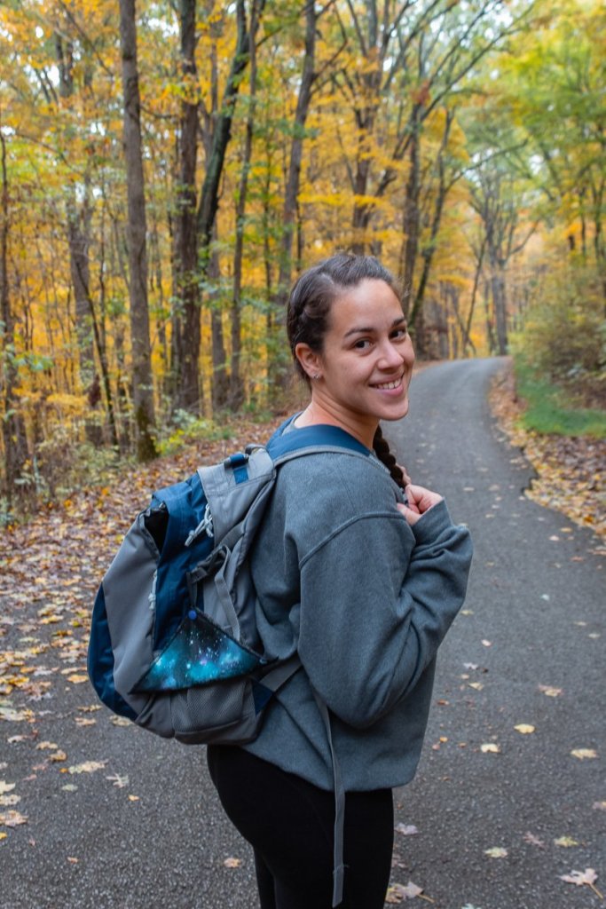 A woman hiking through Illinois. She is wearing a hiking backpack with a Kula Cloth hanging from it.