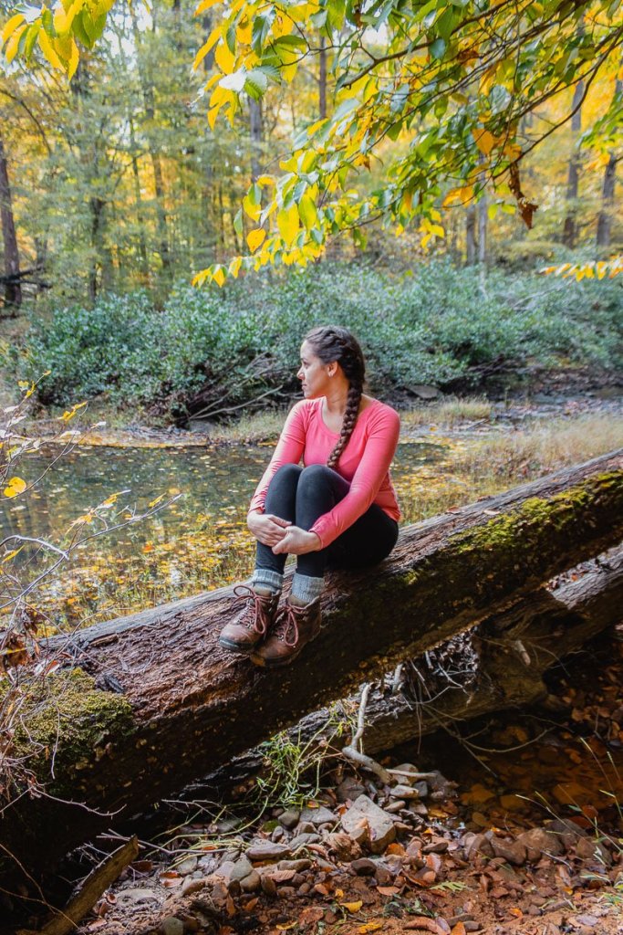 A woman sitting on a log with her hair braided. Posted on a female hygiene guide sharing tips on how to take care of your hair during camping and hiking trips. 