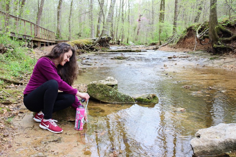 woman getting clean water from a creek while hiking by using the msr gear trailshot water filter