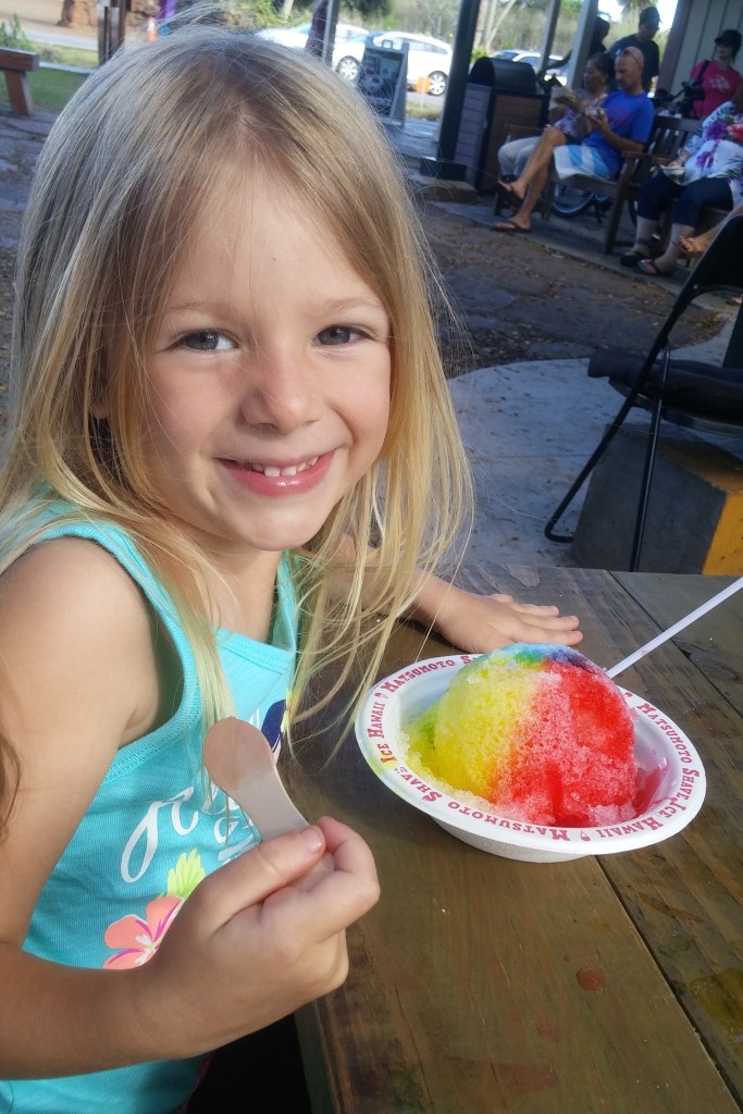 A girl enjoying shaved ice from Matsumoto in Hale'iwa. Posted on a travel guide that features the best things to do with kids on Oahu, Hawaii. 