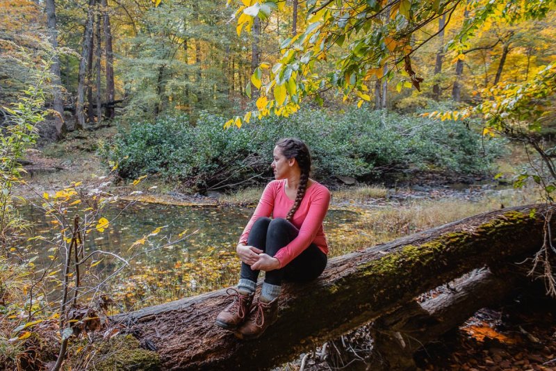 A woman sitting on a log surrounded by Autumn trees in Illinois.