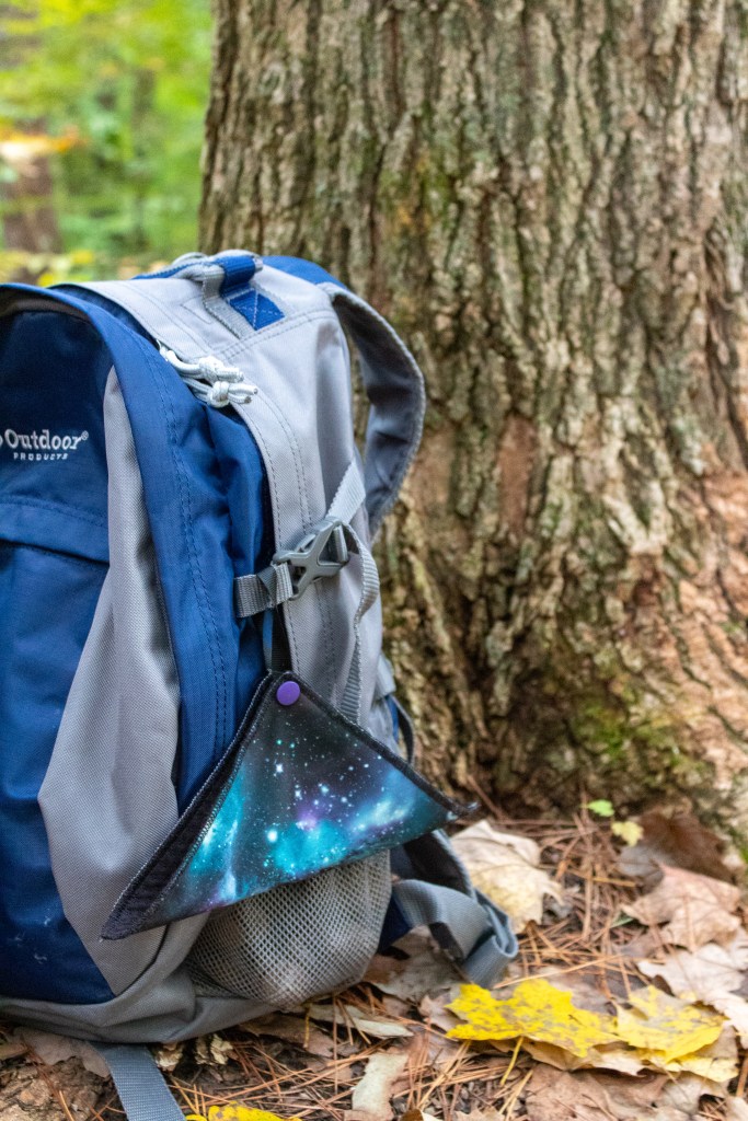 a hiking daypack with a kula cloth on the ground by a tree