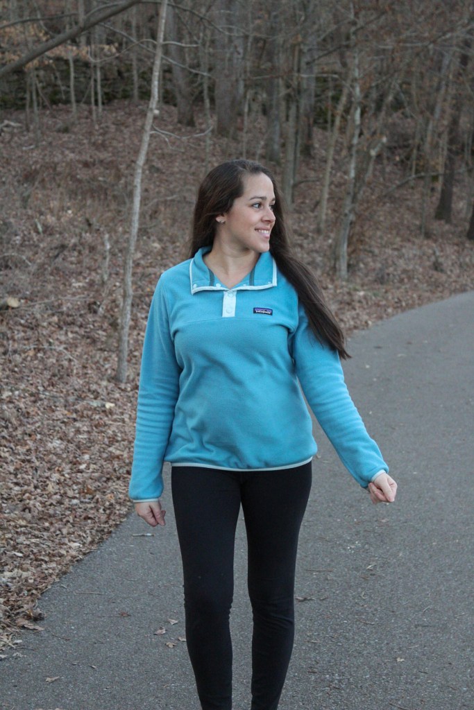 woman wearing a blue pullover fleece jacket and black leggings while hiking outdoors.